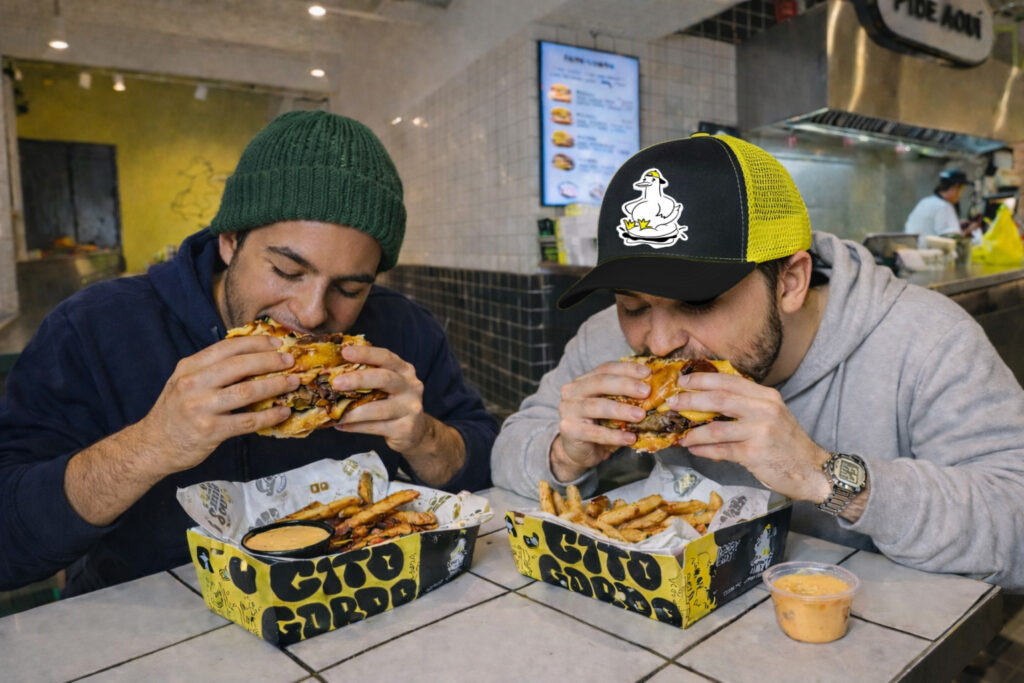 Dos hombres comiendo una hamburguesa en el local de Pato Gordo